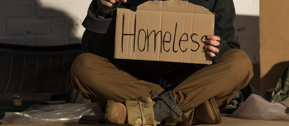 cropped view of homeless man holding piece of cardboard with"homeless" handwritten inscription