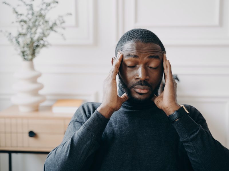 Stressed young african man employee with frustrated face expression suffering from headache